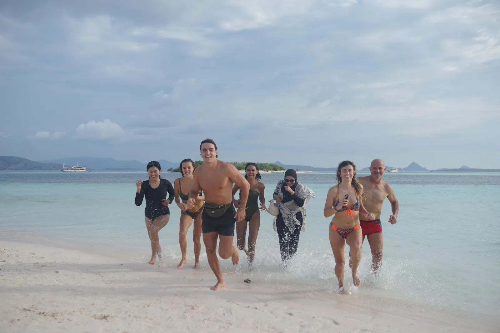 Guests running into the shallows from a white-sand beach in Komodo National Park