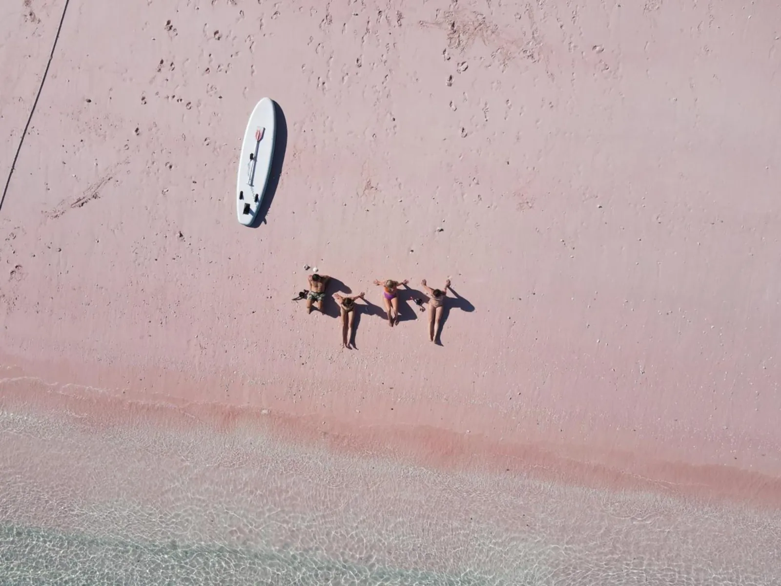 Aerial view of travellers lying on the pink sand at Pink Beach