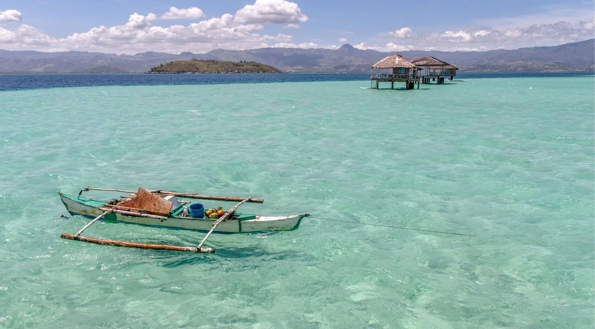 Traditional outrigger boat floating in clear turquoise shallows near Komodo